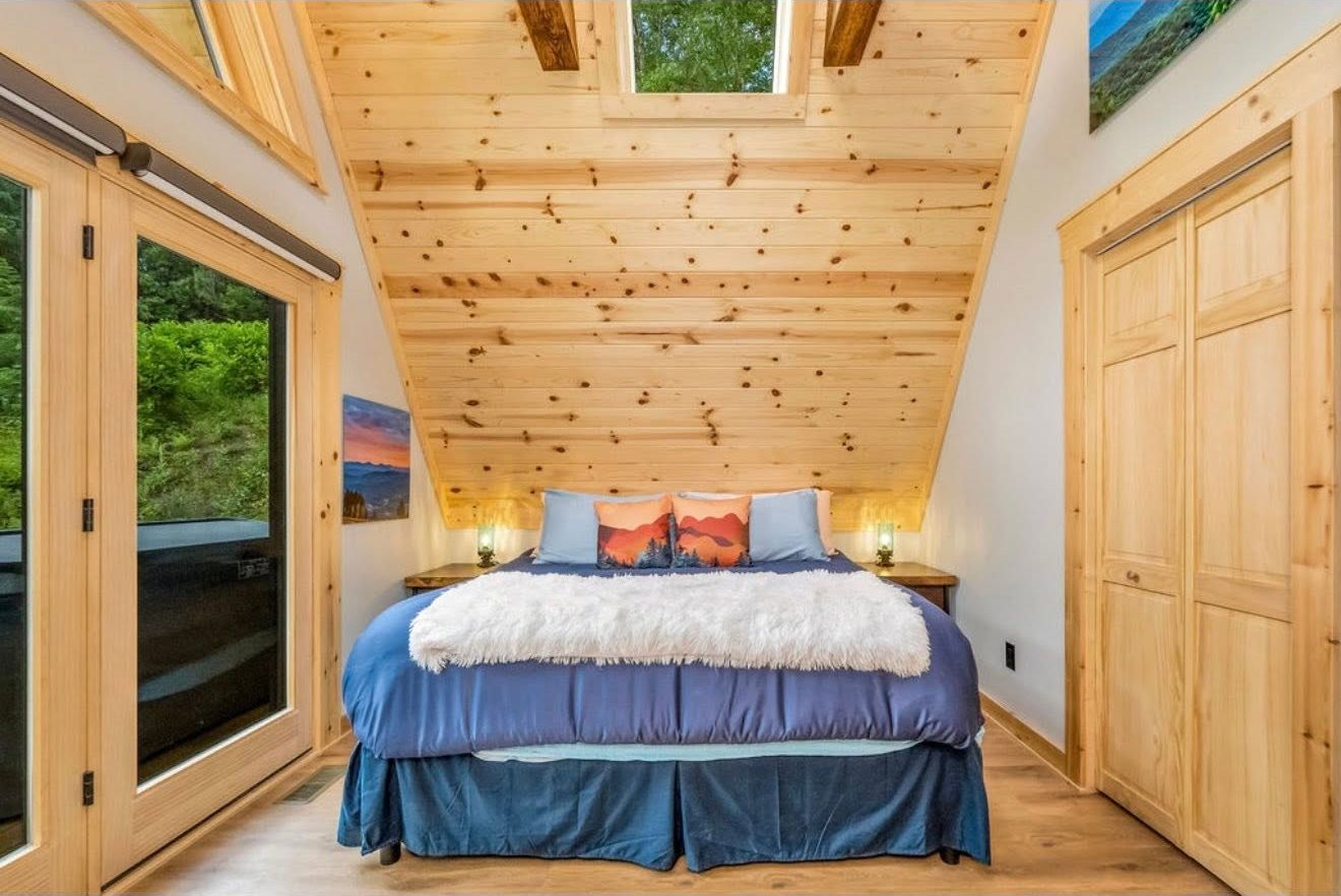 The cabin bedroom under a pine vaulted ceiling
